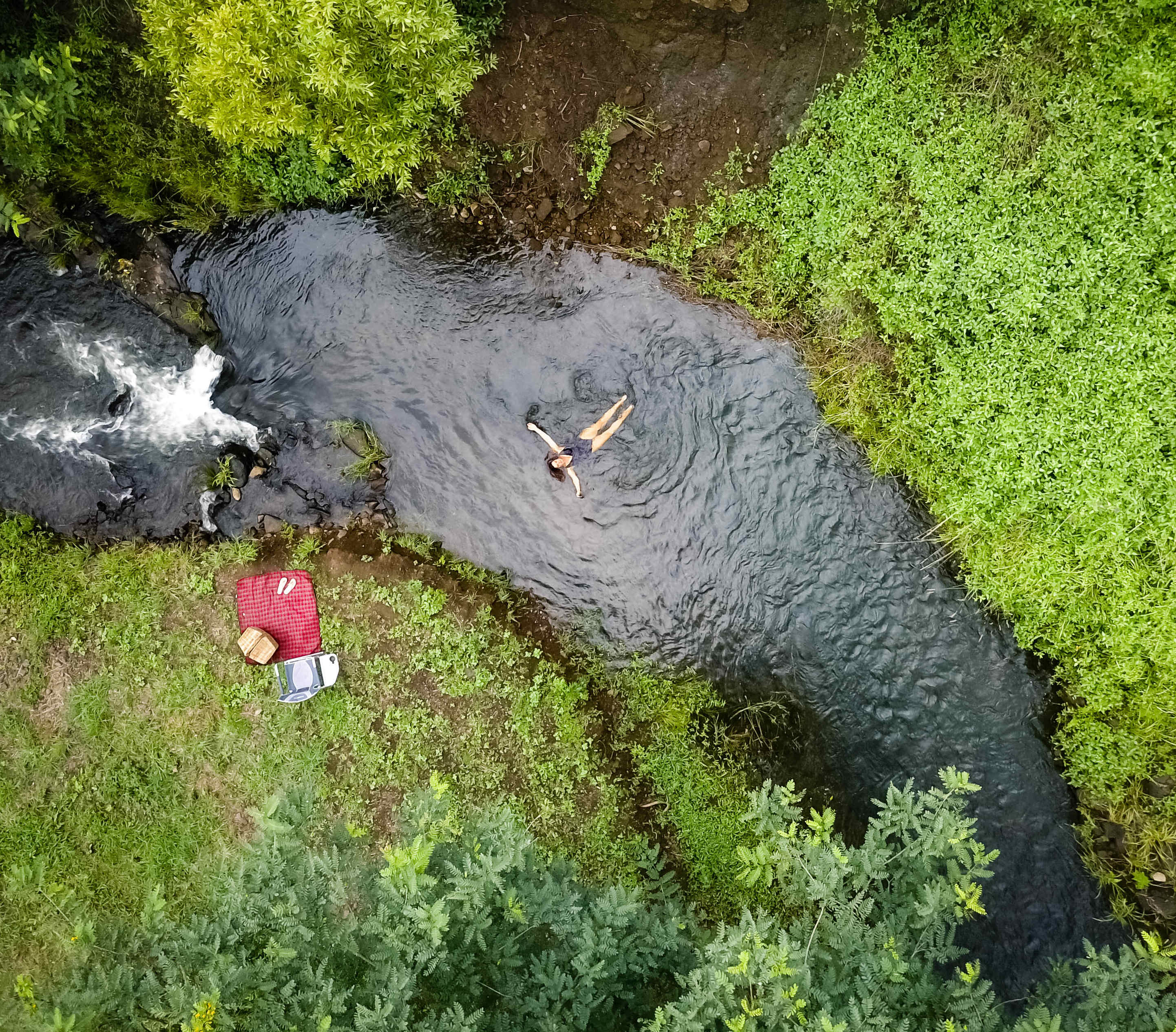 Aerial view of a swimmer in a creek beside a campsite