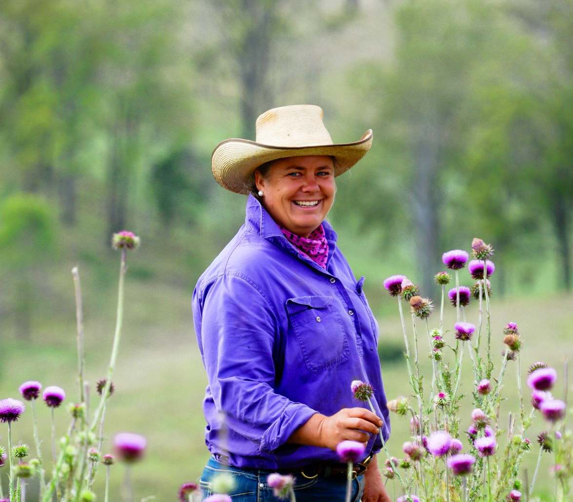 Host in a wide-brimmed hat standing among purple thistles