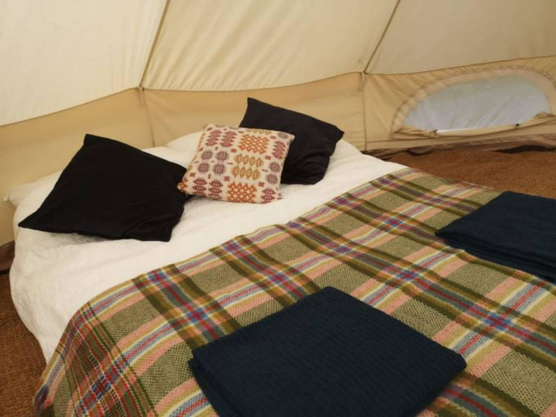 The 5m heated bell tent is furnished with a double and two single futons, made up with fresh, clean linen, duvets, pillows and woven Welsh carthenni blankets. 