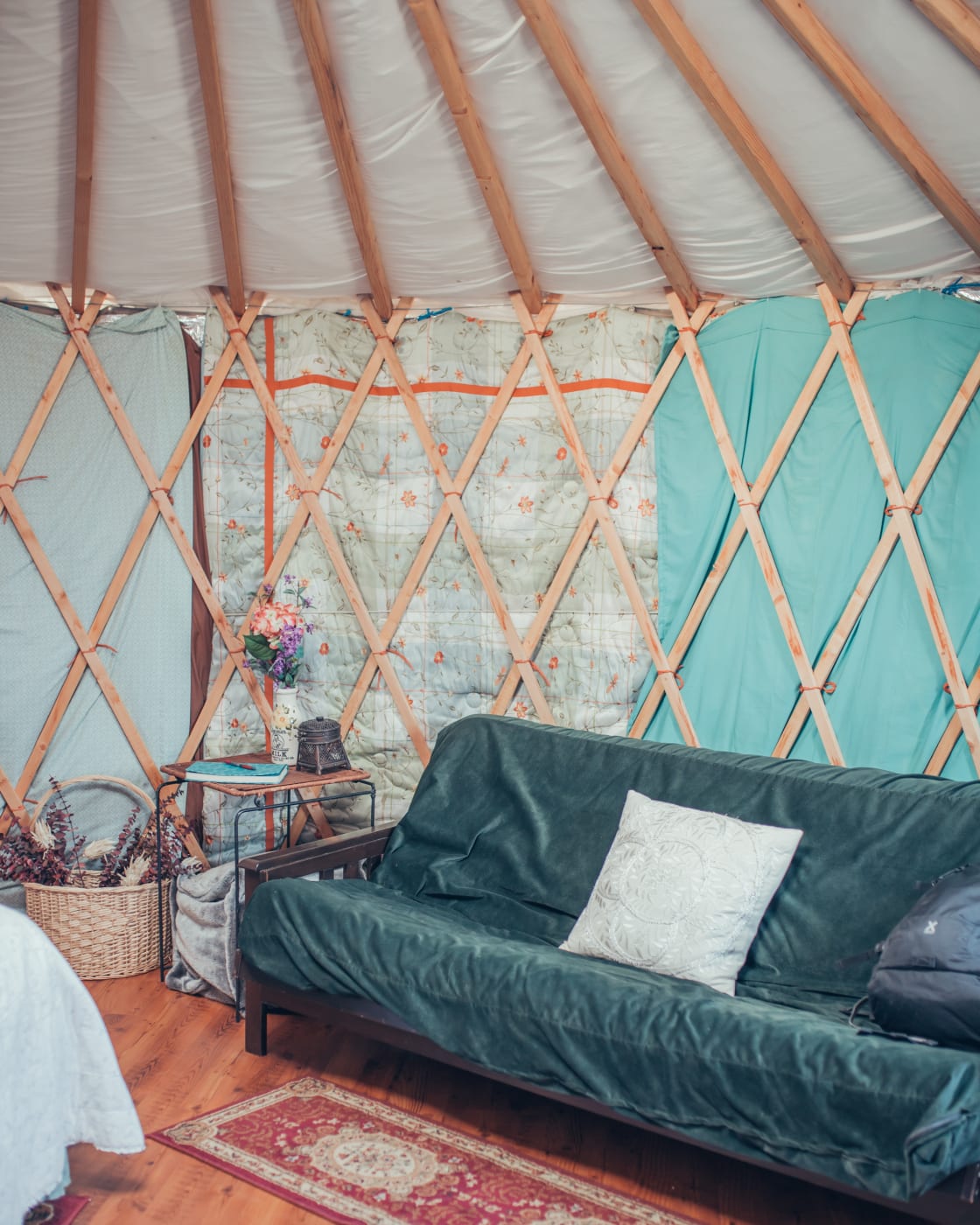 The cozy interior of the yurt features a table and chairs, a futon couch, a queen bed, lanterns for light, lots of blankets, powerful propane heaters, a camping stove, and cookery!