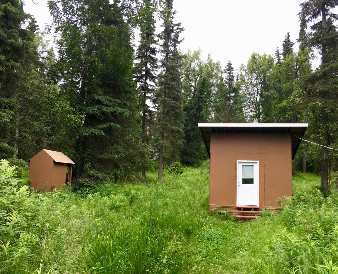 An outhouse is conveniently located to the left of the cabin