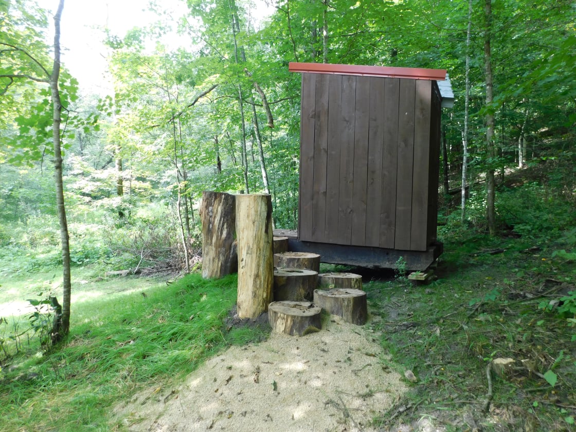 outhouse and log steps leading up to doorway. This is a sawdust - compost toilet with toilet paper provided.