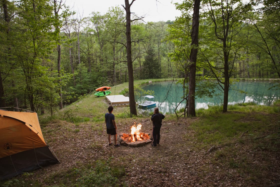 View of the campsite, fire pit, and pond with kayaks and paddle boat available to use!