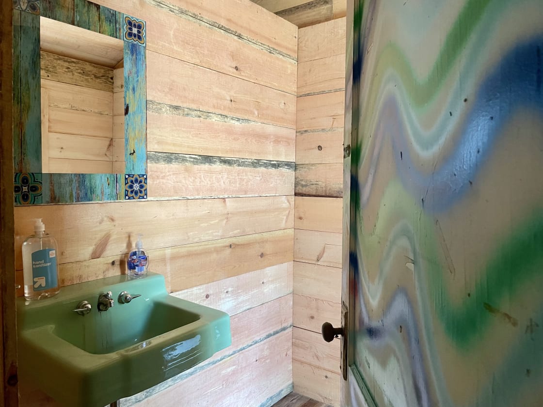 Toilet room in commonground/bathhouse. Vintage hanging sink should be able to accommodate a wheelchair underneath. Large area for wheelchair turn radius as well. 
