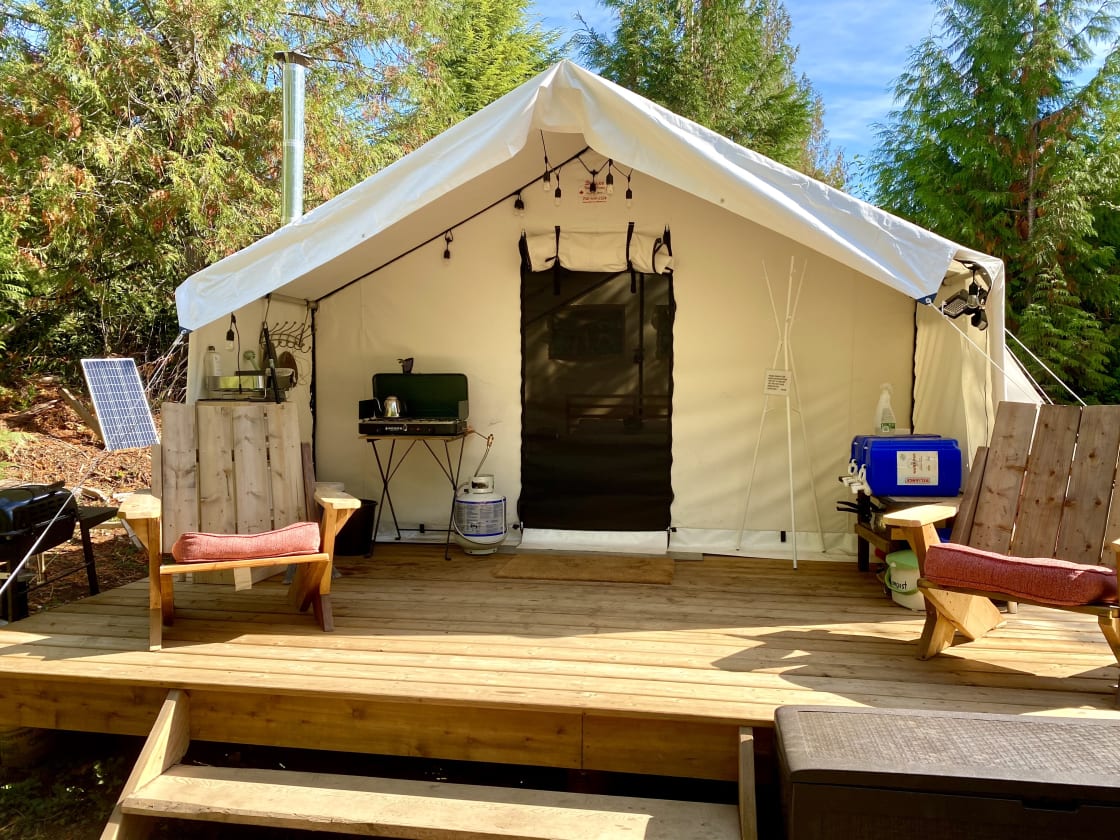 Beautiful glamping tent on a large deck in the woods with covered outdoor kitchen area