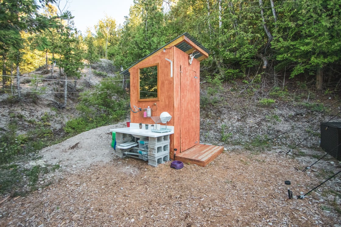 Outhouse with composting toilet, sink, and an outdoor shower is located next to the tent