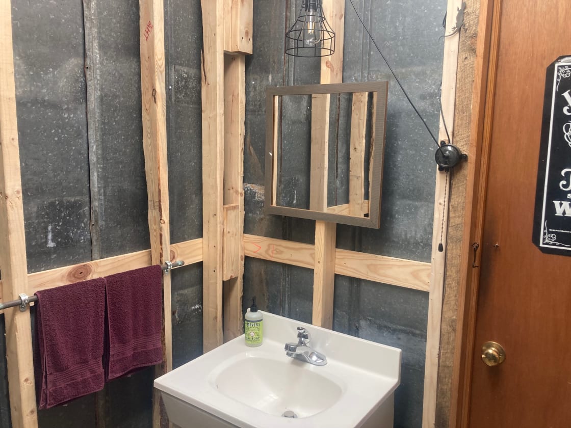 Outhouse interior with foot pump sink, solar light, towels, and hand soap