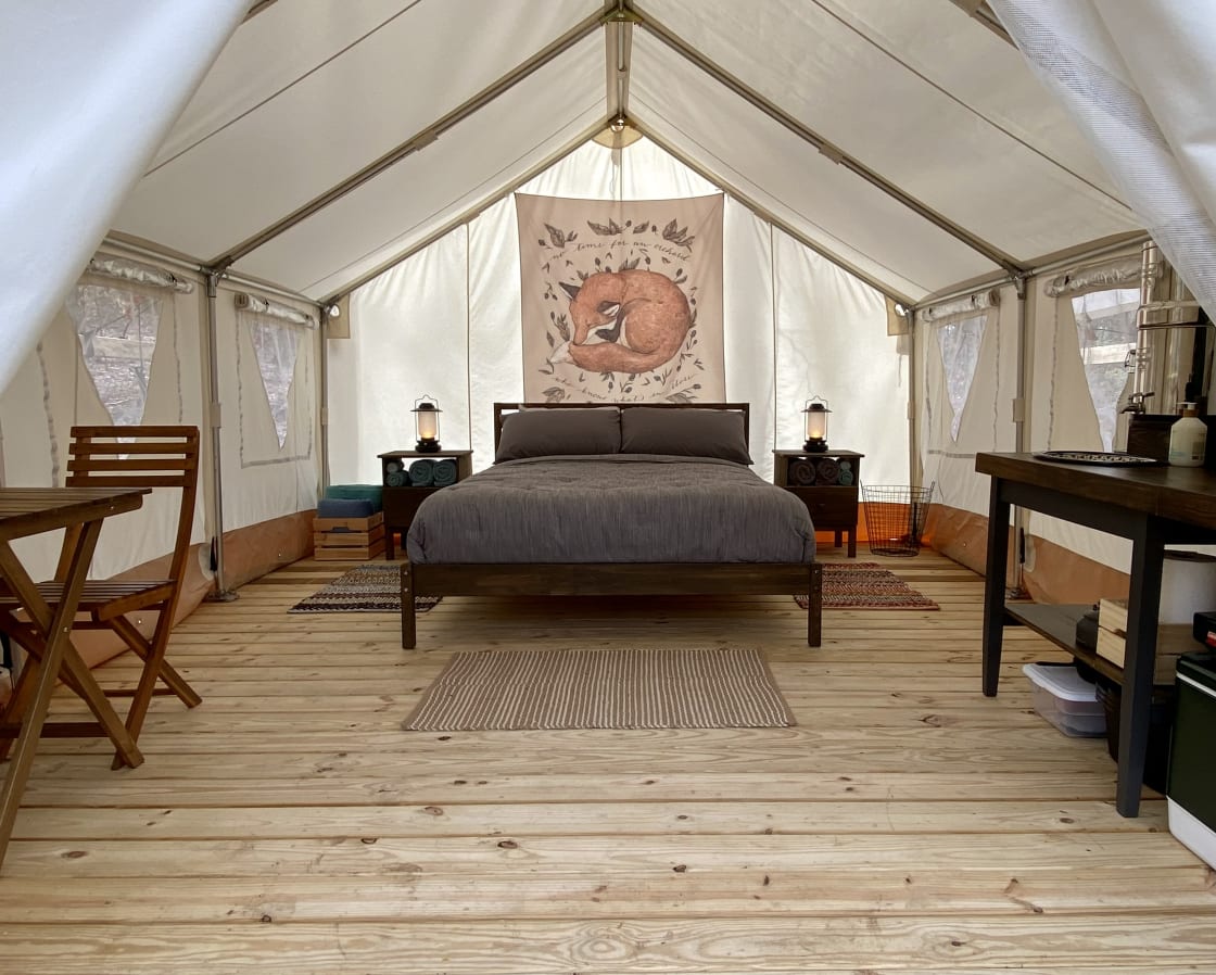 The interior of the tent has a cozy bed, linens, towels, a kitchenette, a dining table, and plenty of lanterns for lighting. 