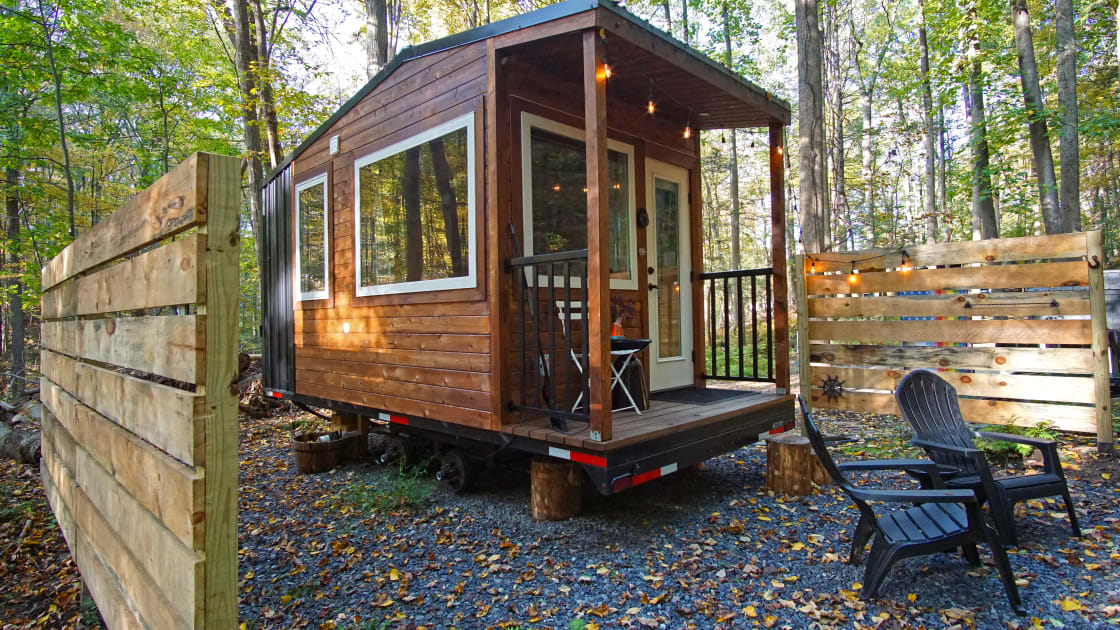Front view of the tiny home with a small porch and seating around the fire pit
