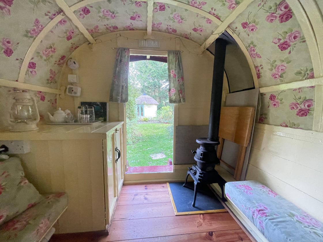 Gypsy Van: view from the bed, showing summer house outside, storage cupboard, bench seats with coordinating fabric and a very cute wood burning stove