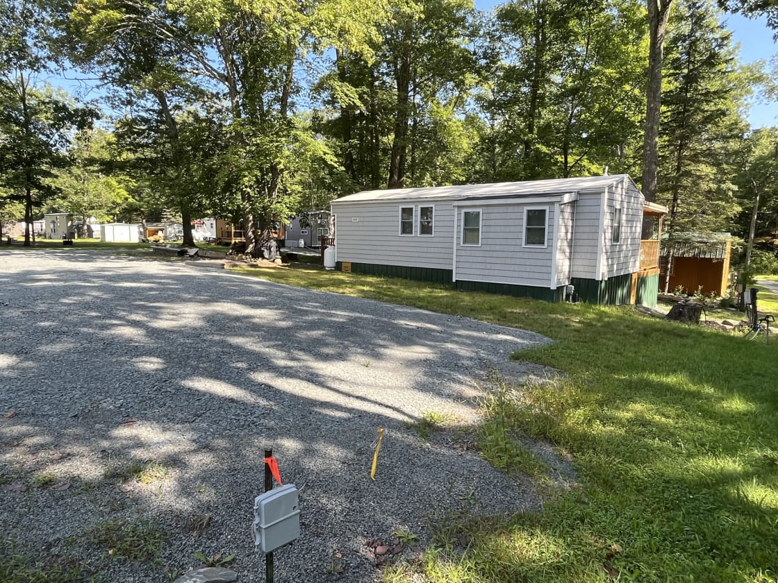 Gravel pad camper site next door to host's unit.  Has picnic table (not in photo) and fire ring.