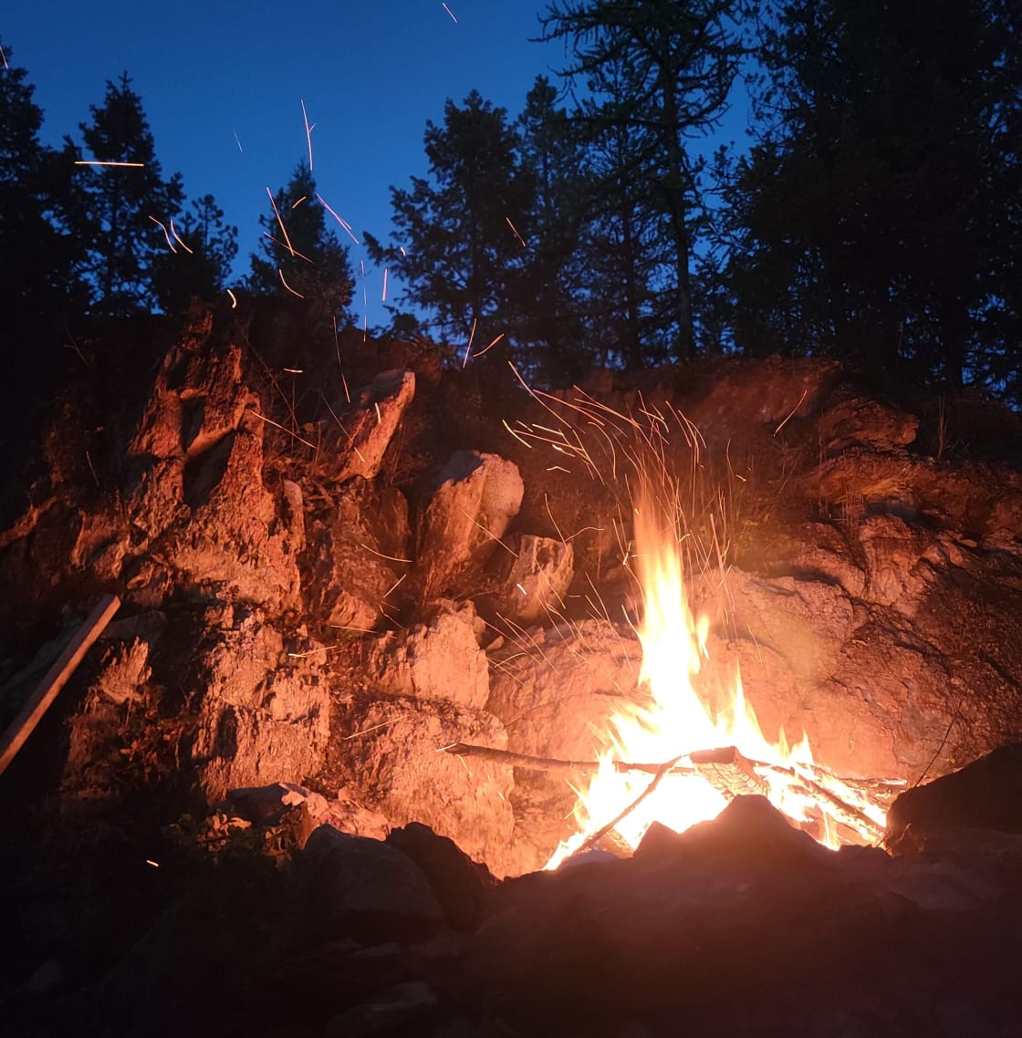 View of the fire pit at night with the natural rock wall behind it.