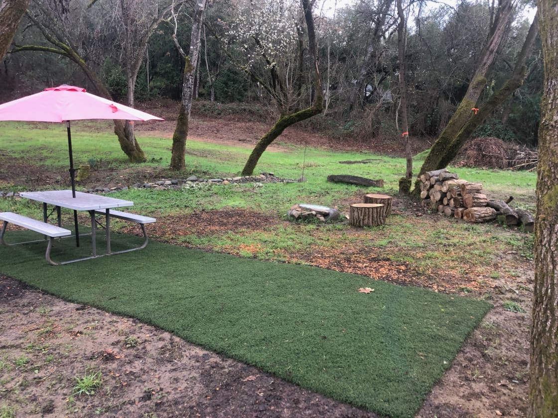 Campsite 1 with firepit, firewood, picnic table with umbrella and artificial grass.