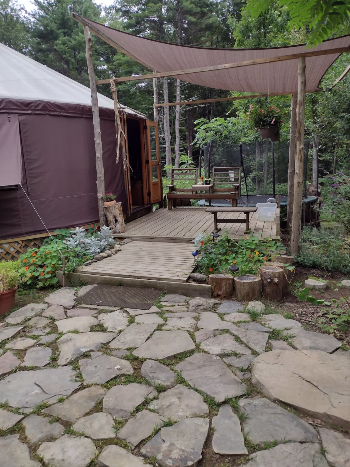 Rock patio leads to the deck surrounded by flower gardens and covered with shade tarp in the summer