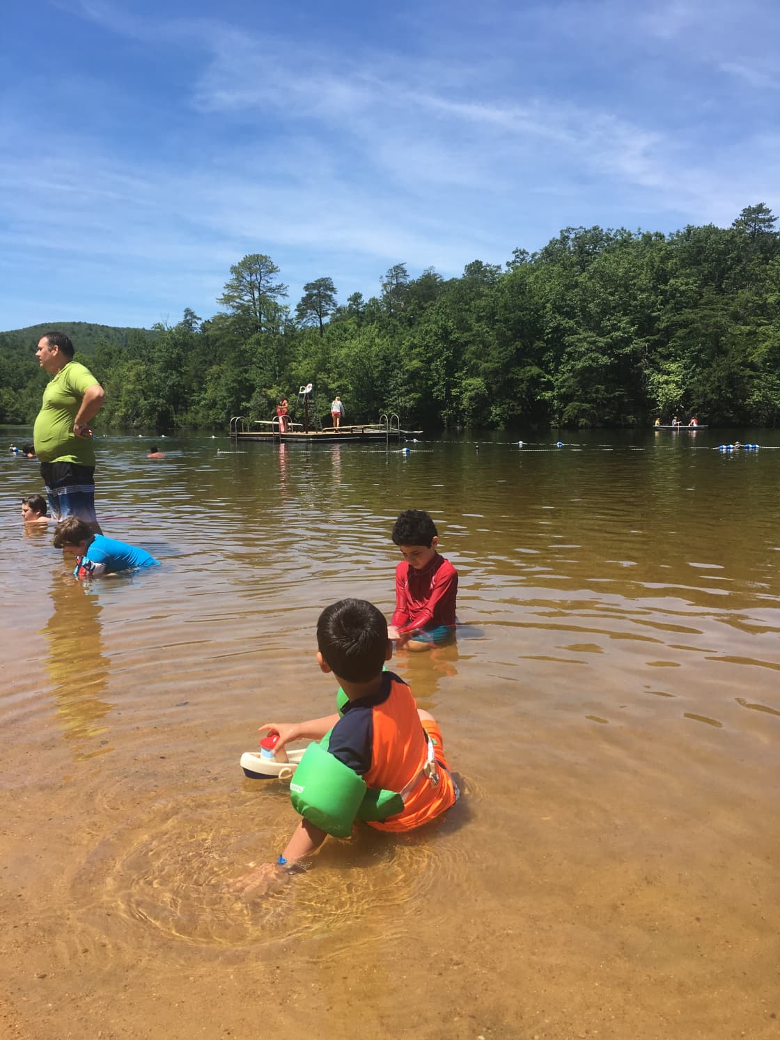 Kids looking for salamanders and small fish at Hanging Rock lake, while visitors enjoy diving off dock in background and rent canoes.