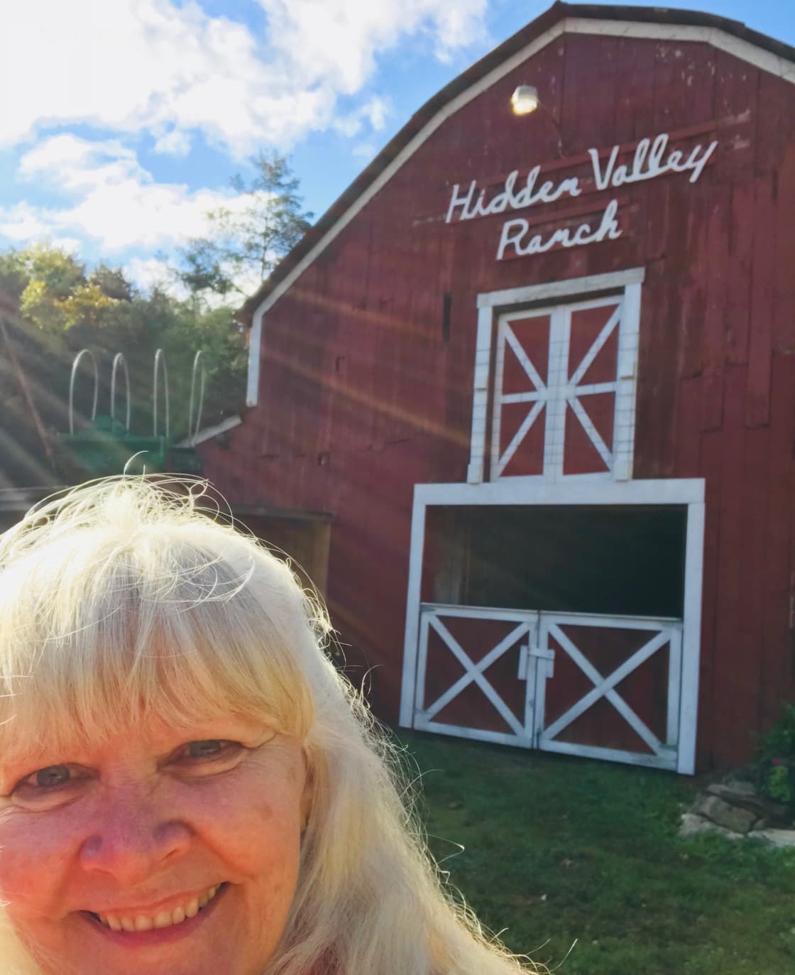 Tandy Belt, hosting Hidden Valley, poses in front of the historic Hidden Valley Barn. She says, “The barn has welcomed so many people (including me) I think she is the actual host!”