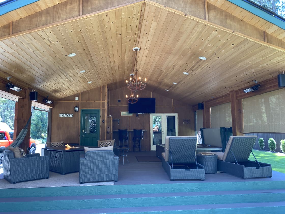 Covered deck with hot tub, fire table, lounges, Bluetooth speakers, heaters, and 65” flat screen TV available for guest use. 