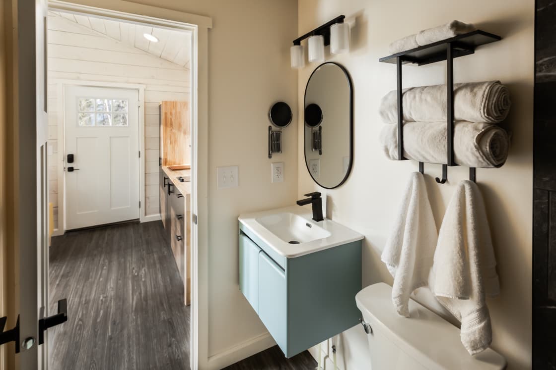 Welcome to the bathroom bash! Check out our snazzy light teal sink and black faucet duo. Towels are ready – rolled or hanging – for your drying pleasure. And don't forget the comfy throne! Let's get this party started!