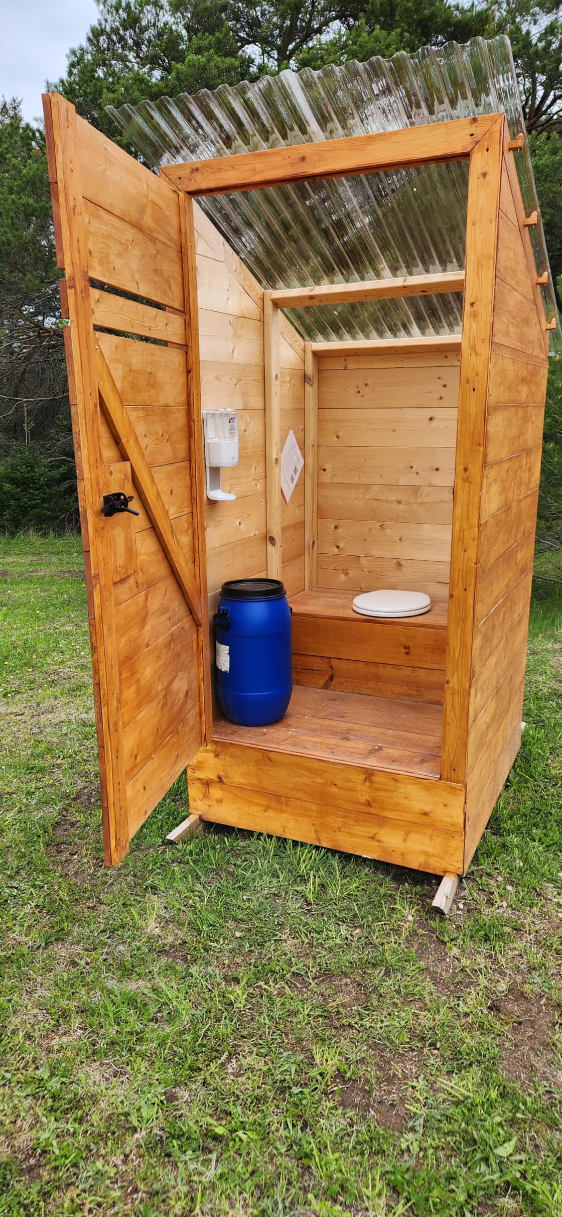 Interior of composting outhouse. Blue barrel holds the sawdust. Hand sanitizer station as well as instructions for the virtual library hang on the wall.