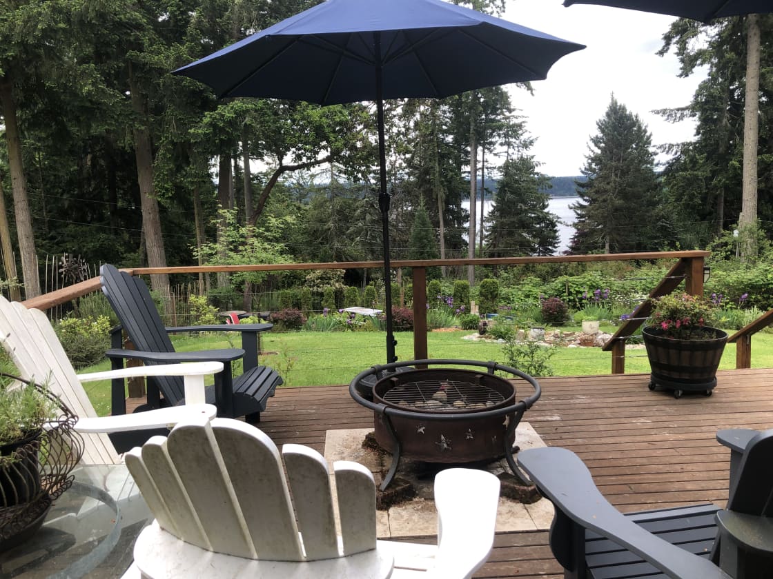 Deck off of the main house with adirondack chairs, fire pits, sun umbrellas and views of the yard and Puget Sound. This is a shared space.