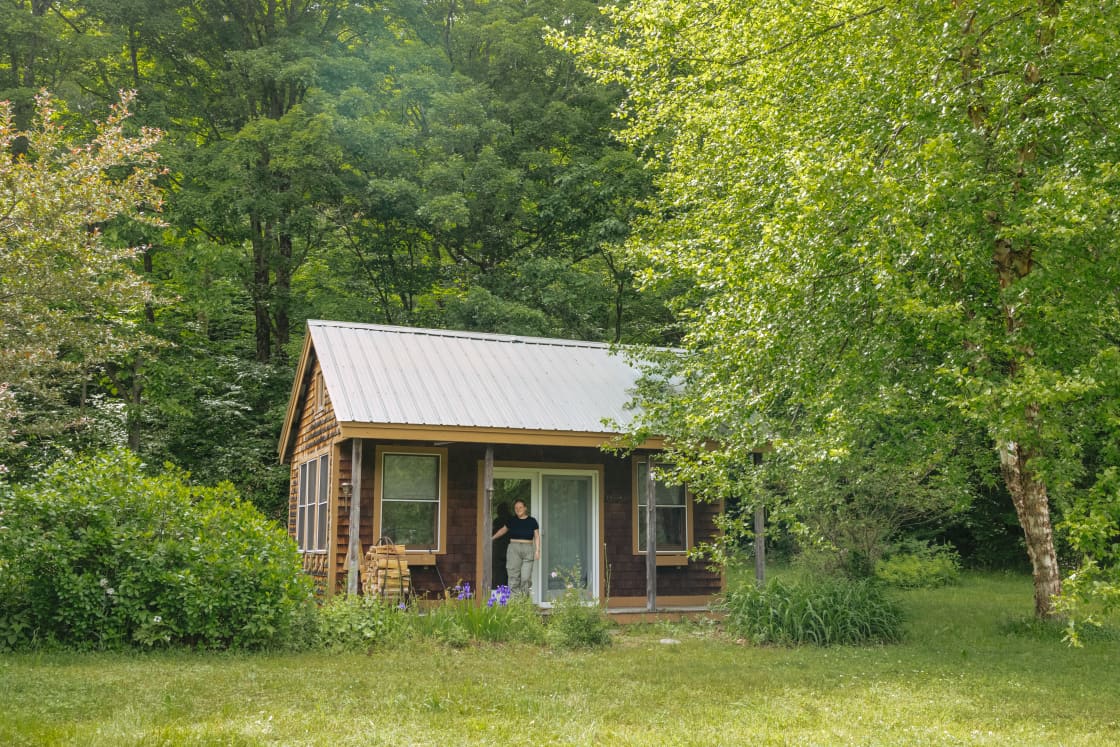 The cabin sits at the top of the meadow tucked against the trees. 