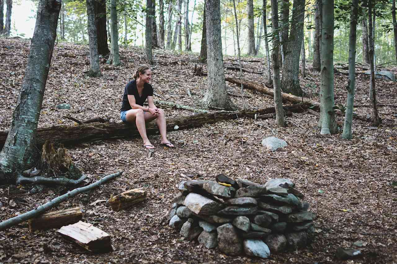 This tent site is nestled in the woods next to boulders and trees.