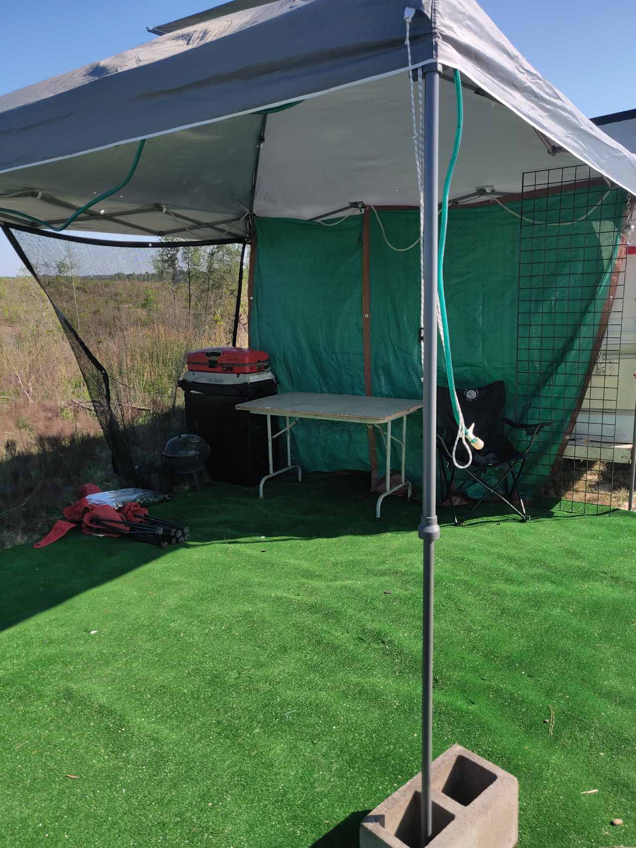 Outdoor lounge and cooking area with small charcoal and gas grill, chairs, table, canopy, and outdoor carpet