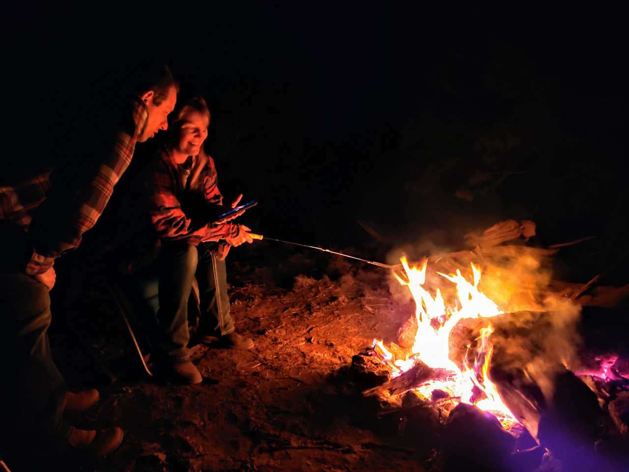 A couple of campers roasting marshmallows and video-chatting with their family by the fire.