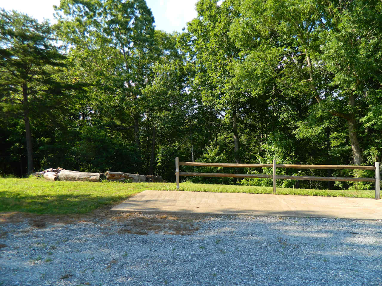 Campsite with concrete pad for chairs and the fire pit in the background to the left.