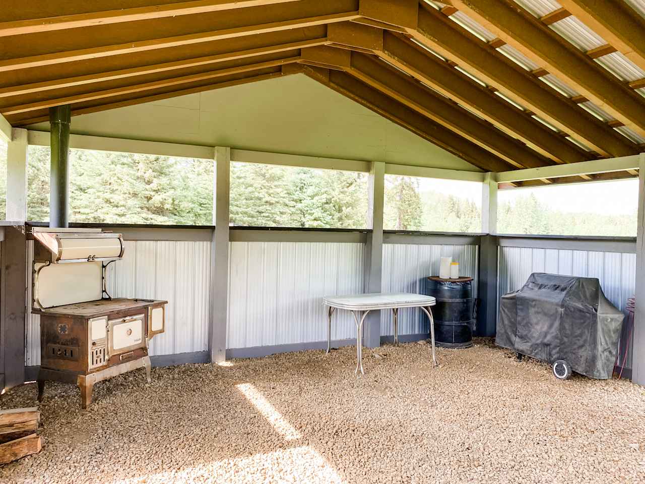 Camp shack interior- equipped with a propane BBQ and firetable, a wood fired old fashioned cook stove, a prep/work table, and a picnic table for dining. 