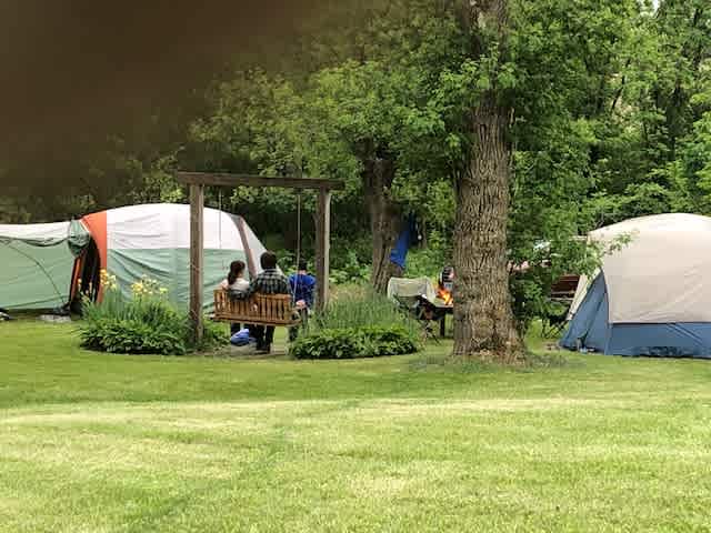 Campers enjoying the porch swing and a bonfire in the shady grove under the trees. 