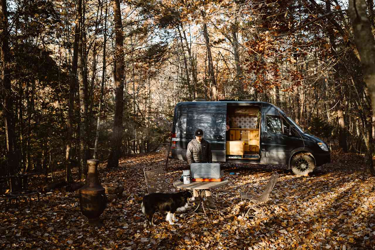 Secluded campsite in the woods featuring a table and chairs set up, firepit & chiminea. Great location for our Sprinter 144 Campervan