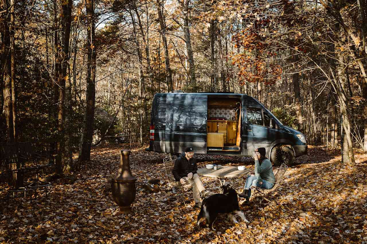 Secluded campsite in the woods featuring a table and chairs set up, firepit & chiminea. Great location for our Sprinter 144 Campervan