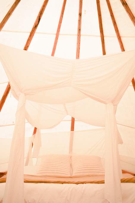 The Tipi is equipped with a bed that is a foldable futon mattress with a white bed canopy.