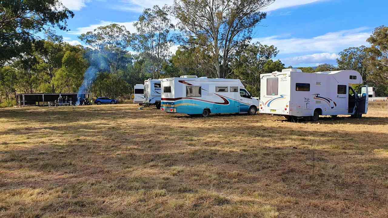 The Grounds campsite is 1.5 acres of level mowed grass. Motorhomes in foreground. Rustic Bar with fire going in background.