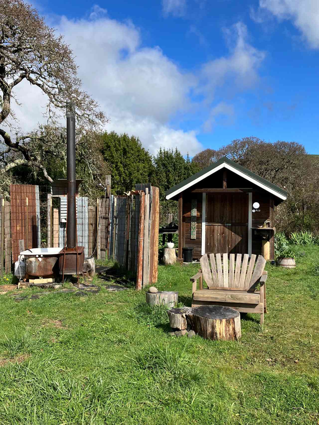 Welcome to The Garden Cabin! Here you can see all outside amenities; shower, bathtub, (the fireplace is merely ornamental) Adirondack love seat, side ‘table’ and foot stool, cabin sink, vanity mirror, pee bucket, and a wide open private space.