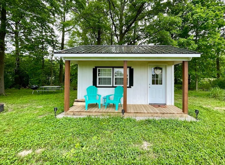 Glamping Cabin #1 with porch chairs, picnic table, charcoal grill, + firepit. Your first round of firewood is stacked for you as well!