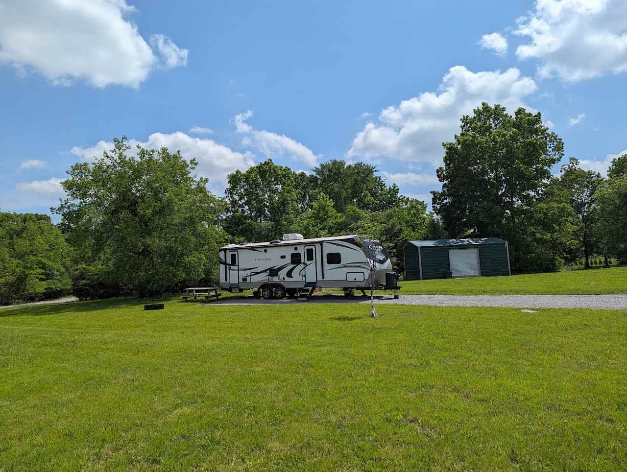 South facing view showing a 34' trailer backed in. Park bench and fire ring for grilling. WiFi access point is on the exterior of the green shed in the background for optimal performance.