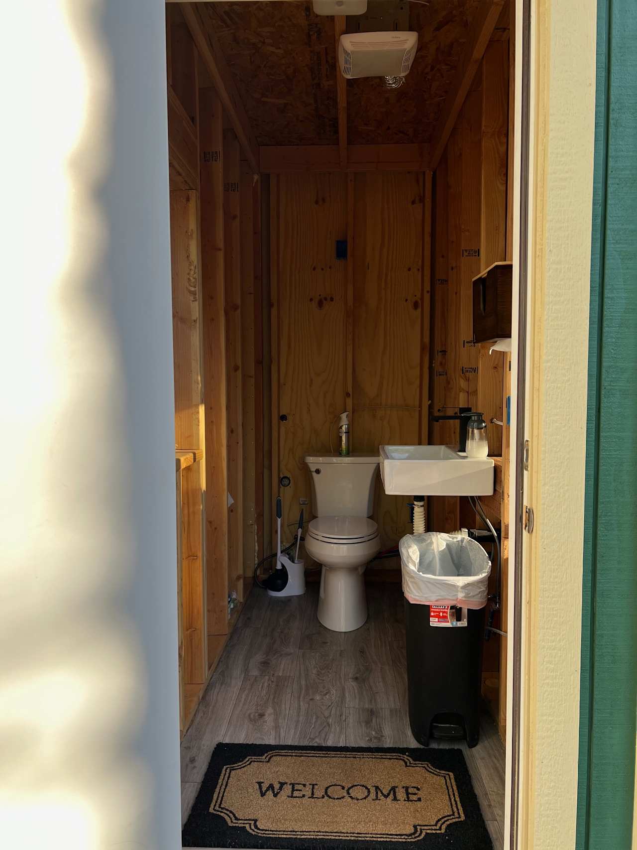 Inside the bathroom house, contains a toilet with toilet paper, trash can, a sink with hand soap and paper towels. 