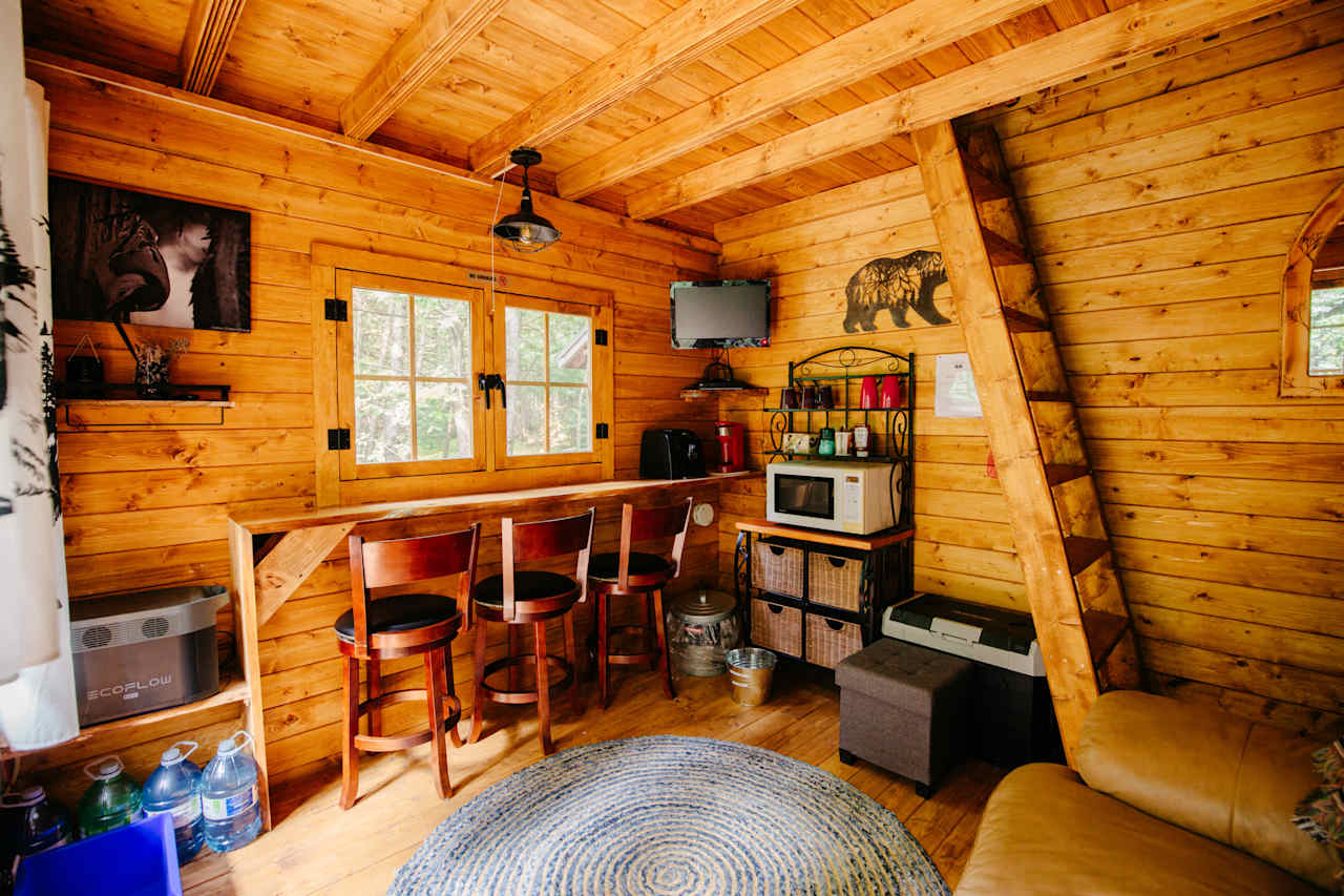 Interior of the bunkie, with the ladder leading to the loft. This cabin is powerd via solar and comes ready with a fridge/freezer combo, and TV!