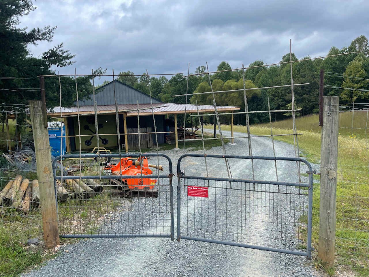 Main gate from the vineyard to the camping area.  Common area with Portolet and picnic table under awning are visible.  Gravel drive leads to the campsite