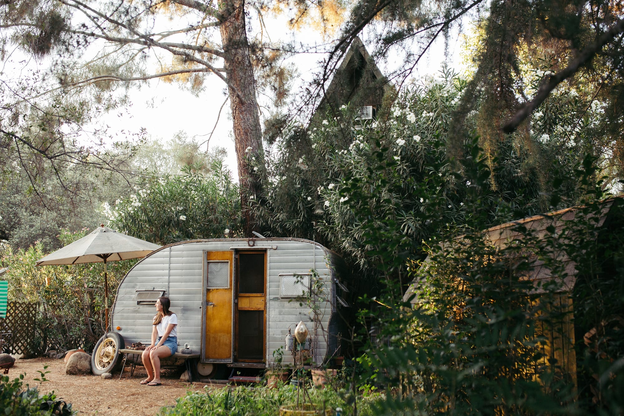 The trailer is nestled between an abundance of greenery and the A-Frame cabin.