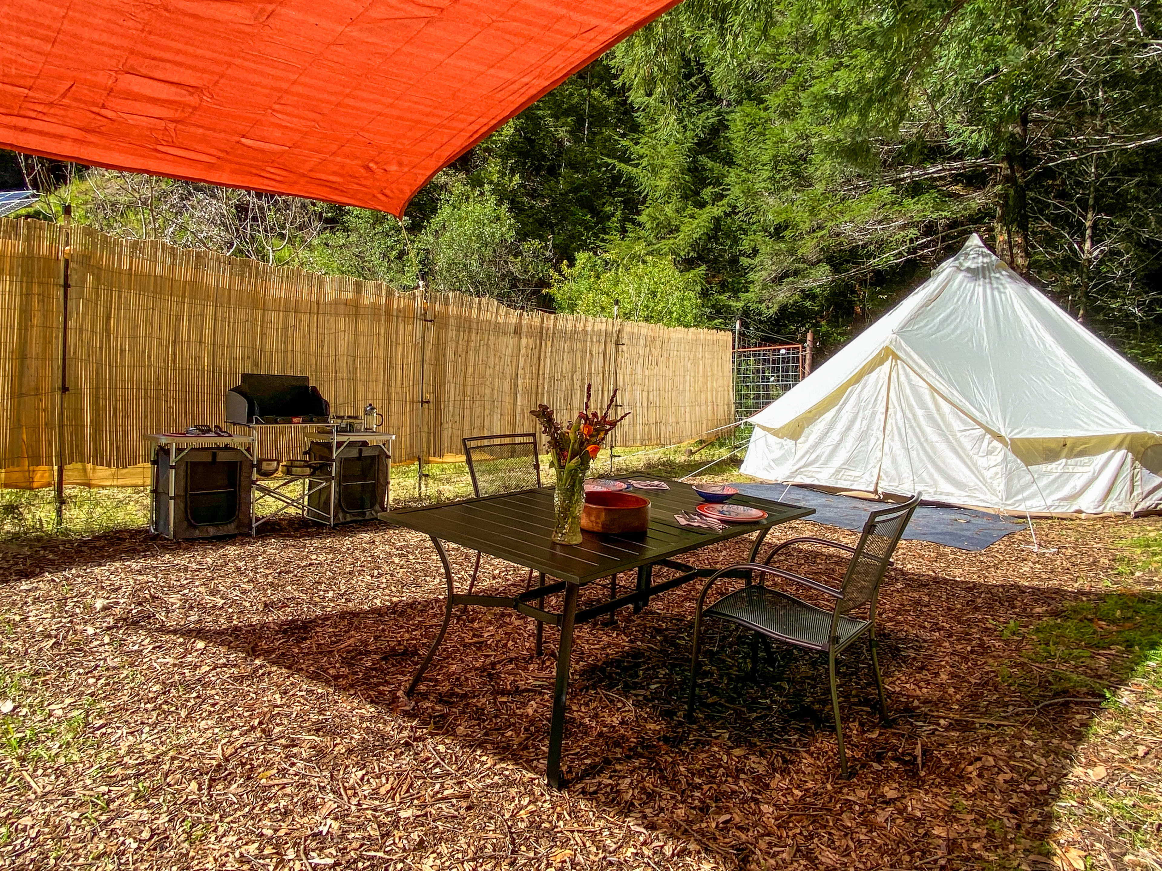 The Orchard Site has a 16ft diameter round tent, privacy fencing, an outdoor kitchenette with a 2 burner propane stove, table, and shade structure.