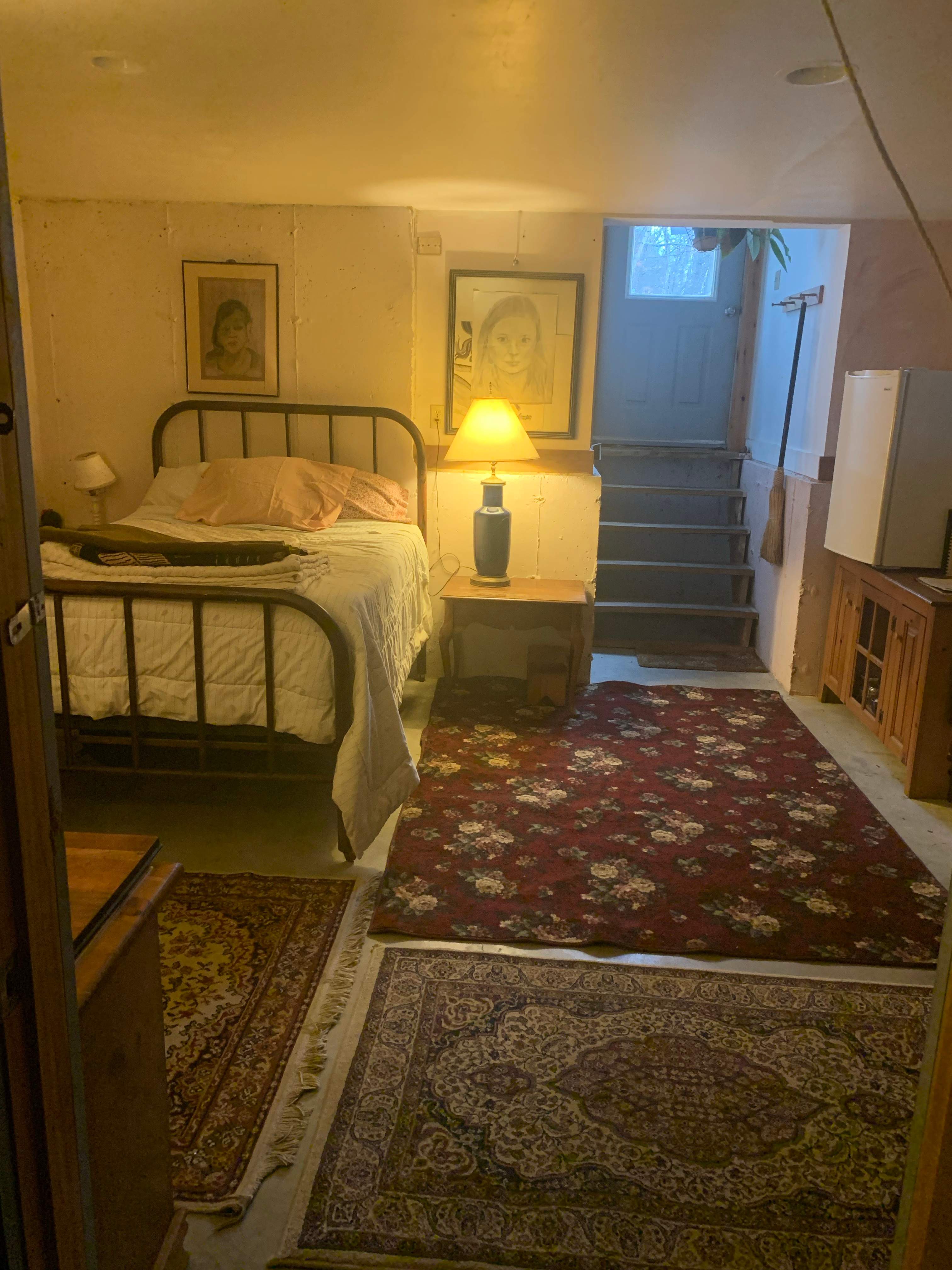 Double bed in a walkout basement room. Simple kitchen to the right. 