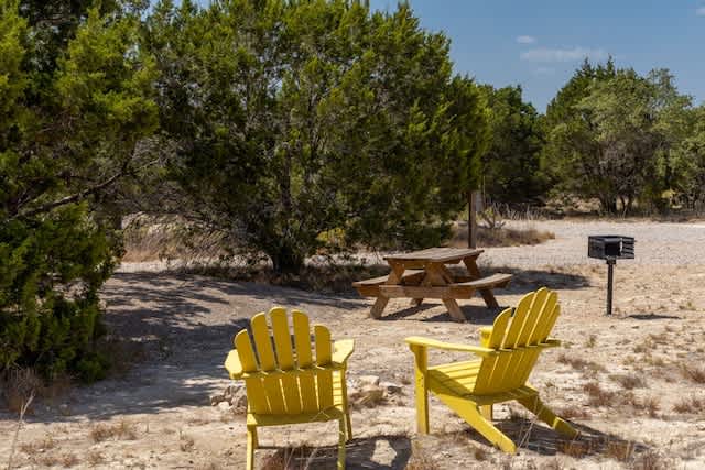 Mulched Campsite nestled in the trees with Adirondack chairs, picnic table, fire pit and grill.