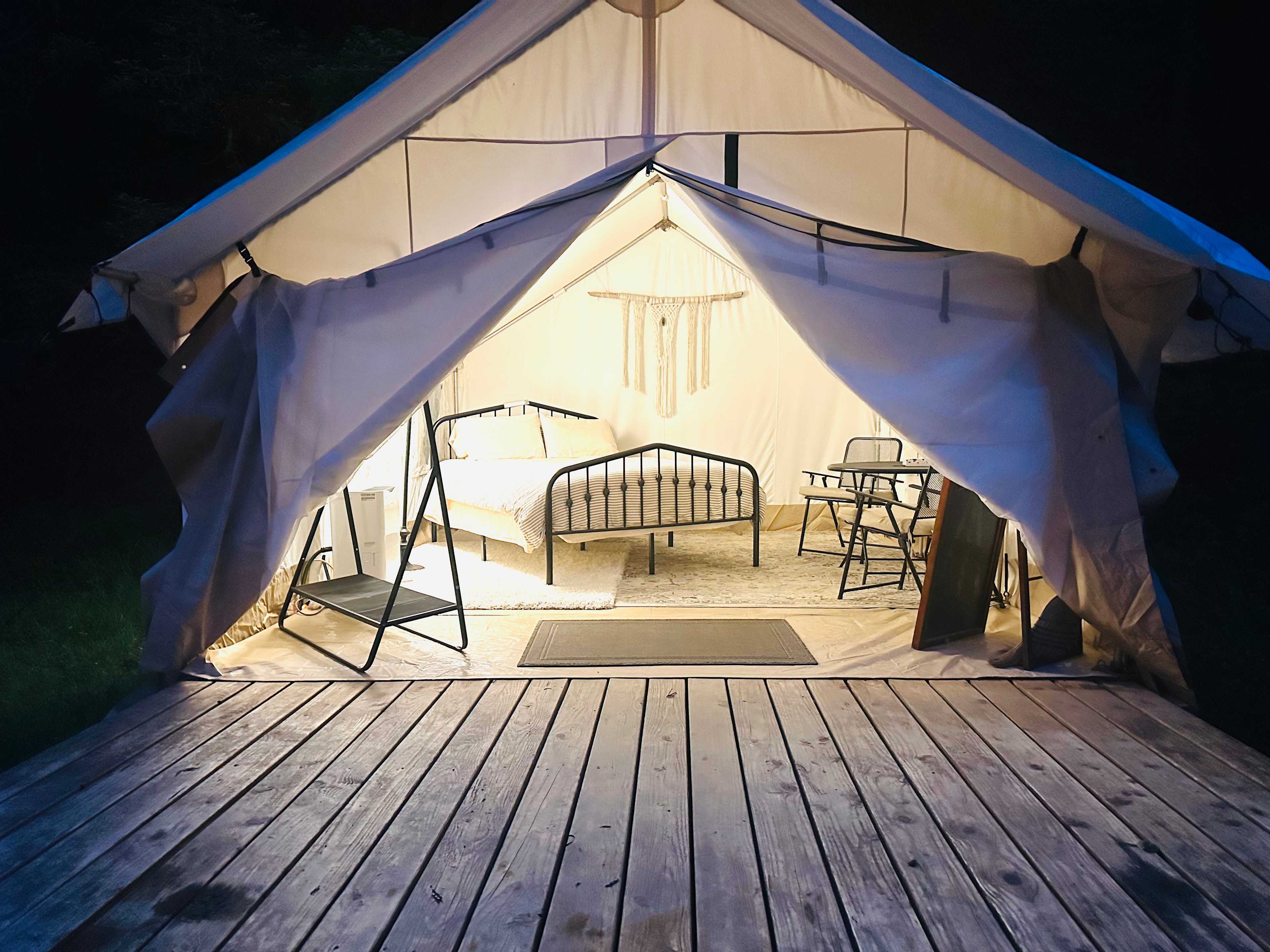 The tent at night with a queen size bed inside, table for two, a mirror, clothing rack, dehumidifier and space heater.