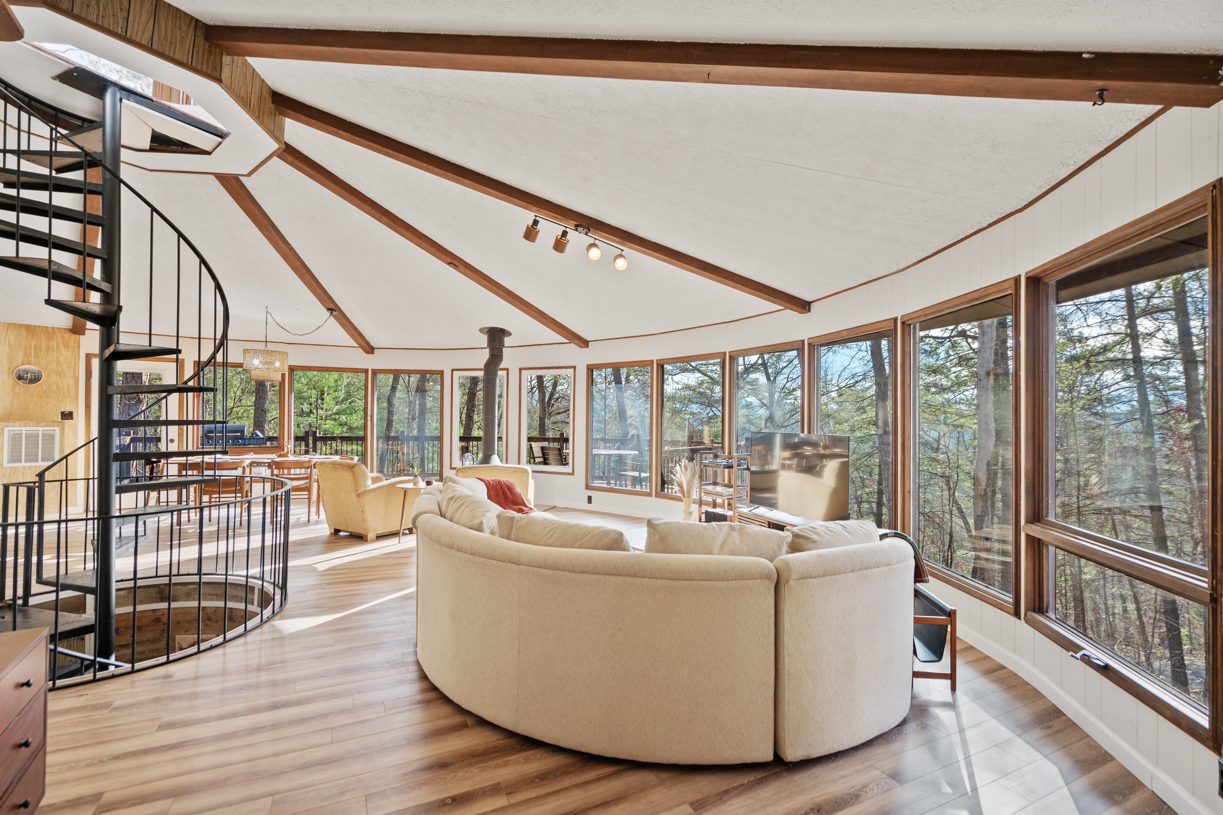 The view of the living room with comfy chairs and couches set up to enjoy the indoor fireplace, TV and views of the forest.