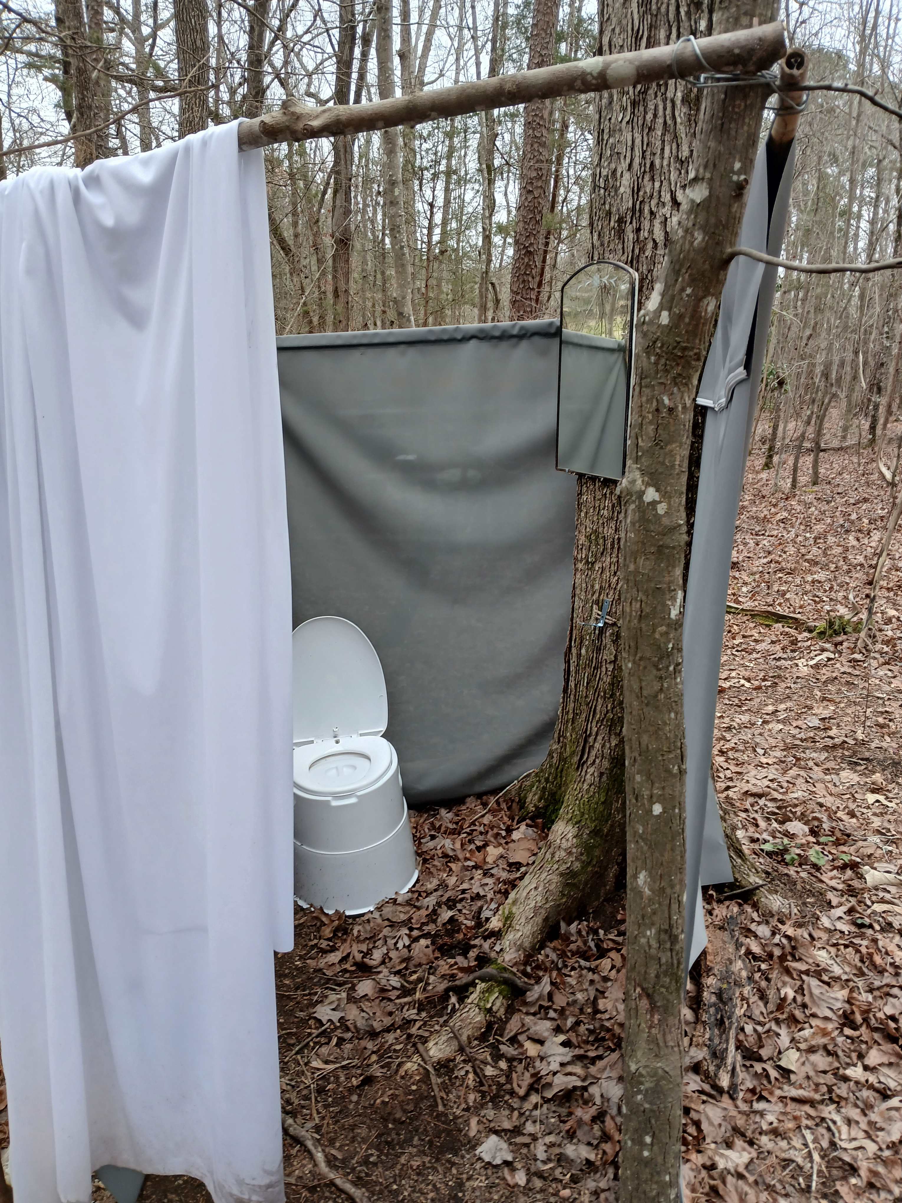 The outhouse style restroom has a toilet and mirror and a place to keep your toilet paper dry.