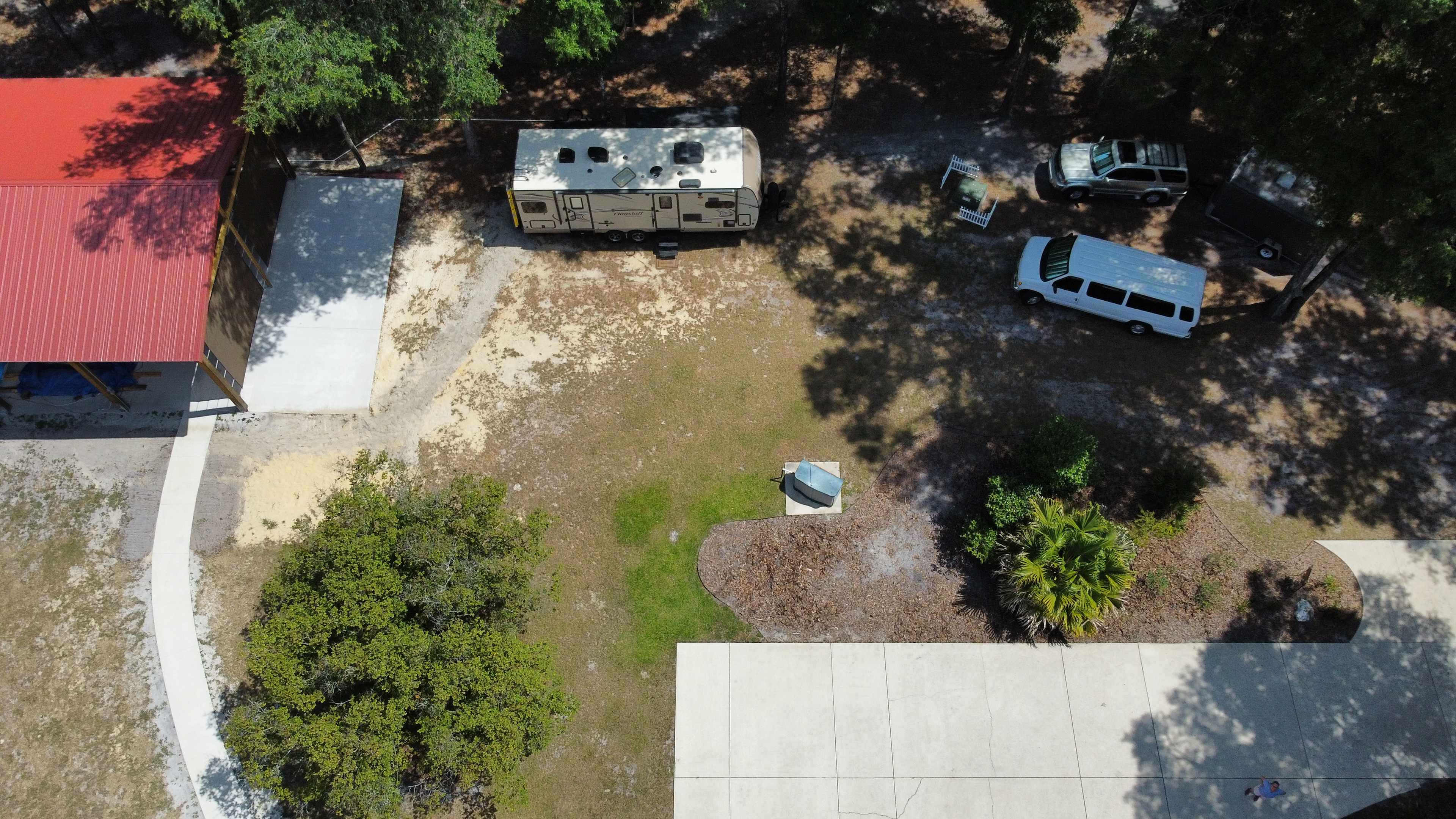 This photo shows a bird's eye view of a camper parked in the Ichetucknee Site. The Ichetucknee Site has partial shade, and you can park very close to your camper, or you can park on the concrete pad that is next to the house. No camper is parked in the Suwannee Site, but if there was one, you would see the front end of it just to the left of the sidewalk next to the red-roofed barn.