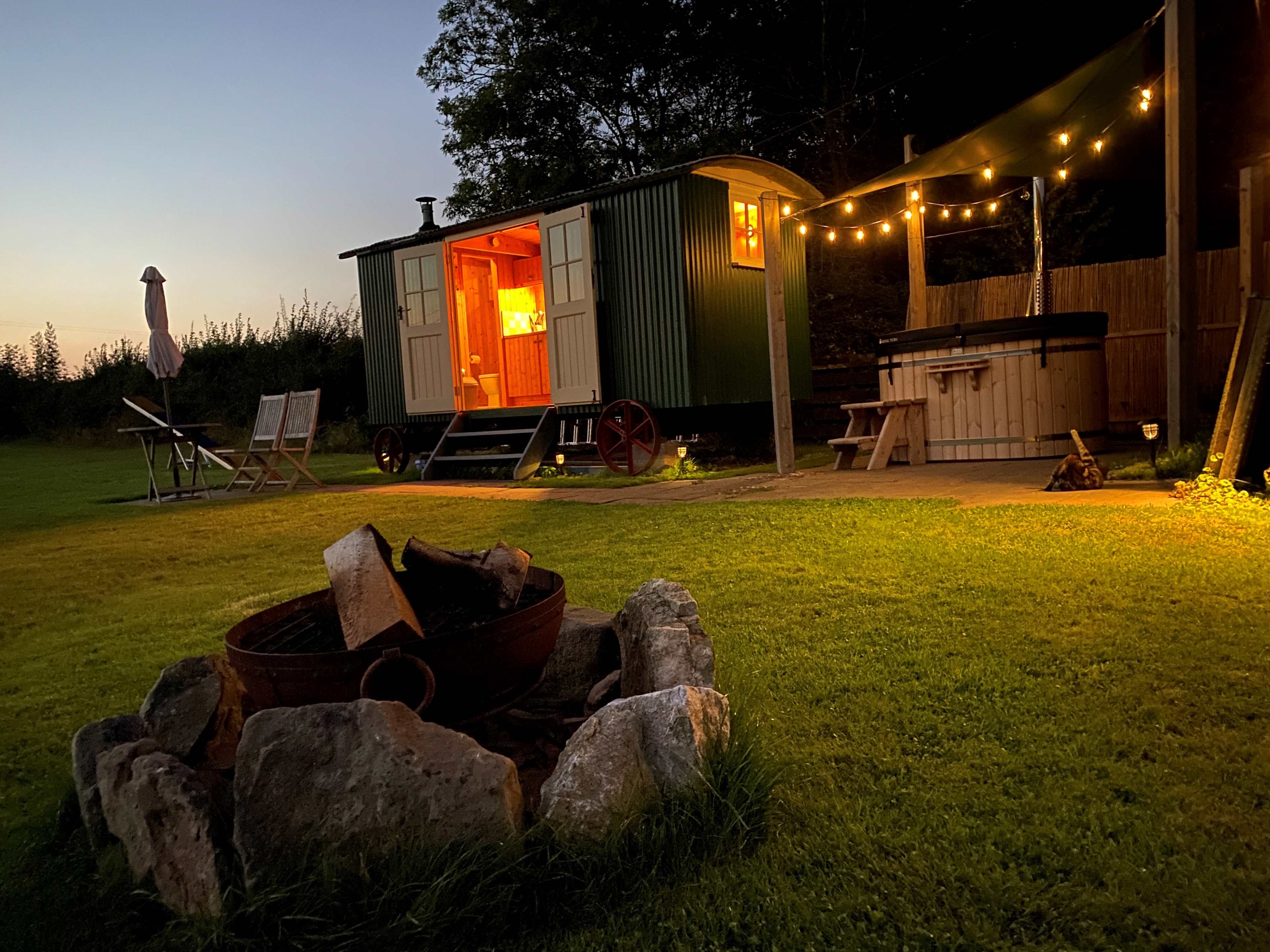 Dusk at the hot tub with festoon solar lighting and firepit in foreground (plus cat!!)